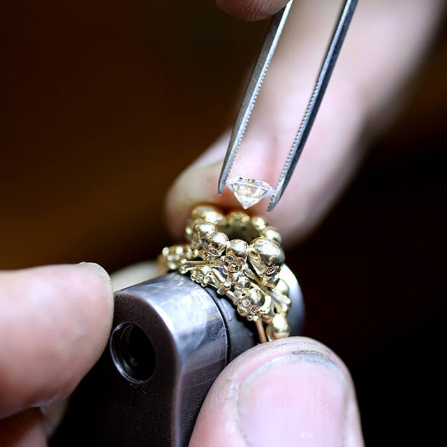 A workshop picture showing a gold ring with a large central stone being set. The stone is being placed with jewellers tweezers.